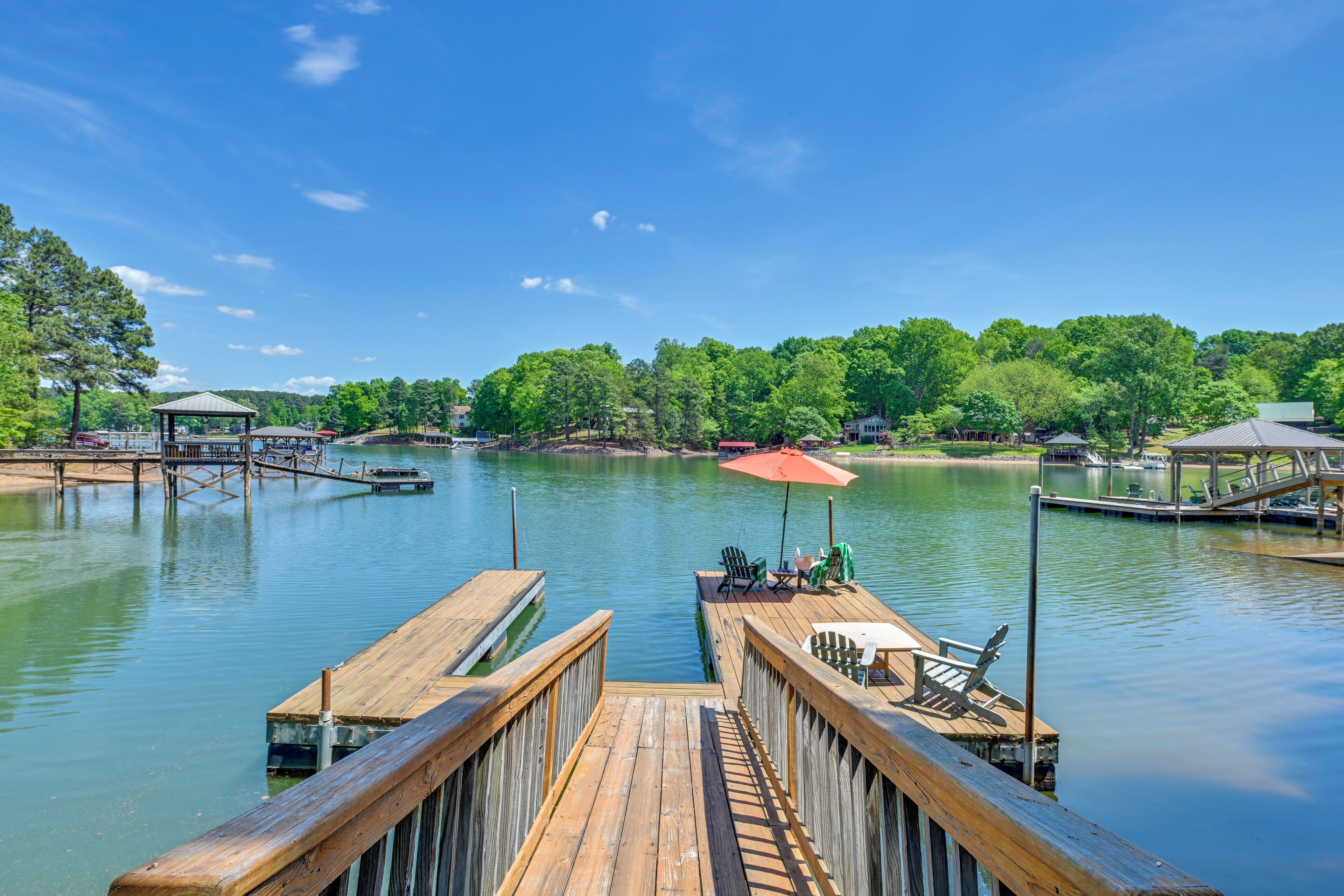 A wooden dock leading to a calm lake with a gazebo and outdoor seating.