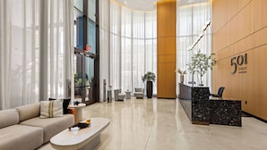 Um saguão moderno de hotel com balcão de recepção, área de estar e grandes janelas.