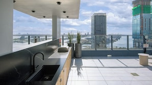Um bar moderno no terraço, com pia, plantas em vasos e vista para o horizonte da cidade e para a água.