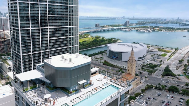 Um hotel alto com piscina no terraço, um edifício grande com cúpula e vista para uma orla marítima com uma ponte.