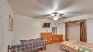 Une chambre avec deux lits, un ventilateur de plafond, une commode, un téléviseur et une porte donnant sur une autre pièce.