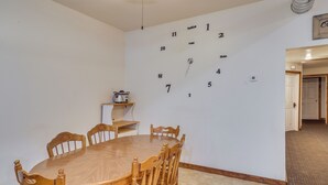 Une salle à manger avec une table et des chaises en bois, une horloge murale et une petite étagère sur laquelle se trouve une radio.