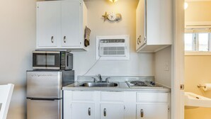 Cocina compacta con armarios blancos, un refrigerador de acero inoxidable, un microondas, una estufa y un equipo de aire acondicionado integrado.