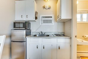 A compact kitchen with white cabinets, a stainless steel refrigerator, a microwave, a stove, and a built-in air conditioning unit. - Old Orchard Beach Condo: Steps From the Beach! (Old Orchard Beach)