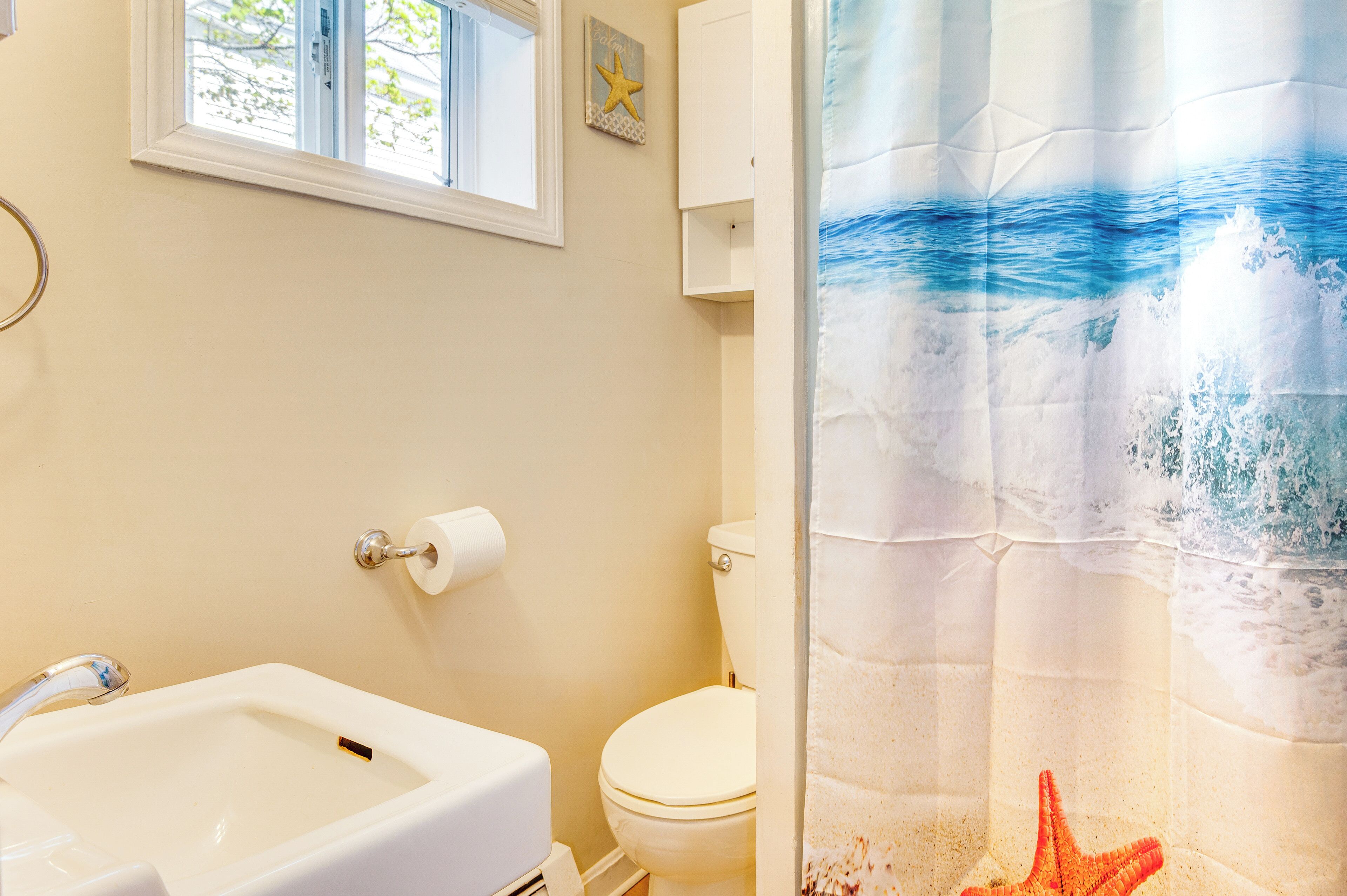 Une salle de bain avec un lavabo blanc, des toilettes et un rideau de douche orné de motifs représentant des vagues océaniques.