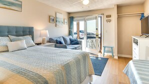 Un dormitorio con cama, escritorio, silla, ventilador de techo y vista a través de una puerta de cristal.