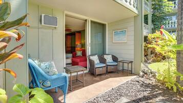 An outdoor seating area with wicker furniture and a small table, a red sofa, and a view of the interior through an open door.