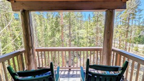A wooden deck with two green chairs facing a forest view. - Private Balcony | King Bed | Near Trails (Keystone)