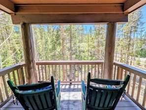 Eine Holzdielen-Terrasse mit zwei grünen Stühlen, die auf einen Blick ins Waldgebiet ausgerichtet sind.