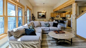 A spacious living area with a large sectional sofa, a round coffee table, and a kitchen in the background. - Private Balcony | King Bed | Near Trails (Keystone)