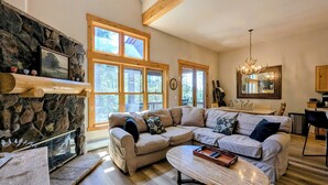 A cozy living room with a stone fireplace, large windows, a wooden ceiling, and a chandelier. - Private Balcony | King Bed | Near Trails (Keystone)