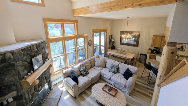 A spacious living area with a stone fireplace, a wooden ceiling, and a dining area with a wooden table and chairs. - Private Balcony | King Bed | Near Trails (Keystone)