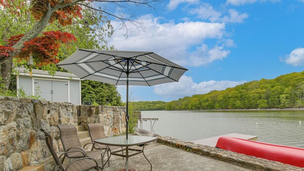 A patio with a table and chairs, an umbrella, and a view of a lake. - Lakefront Bliss in Mahopac! Charming Home w/ Dock (Mahopac)