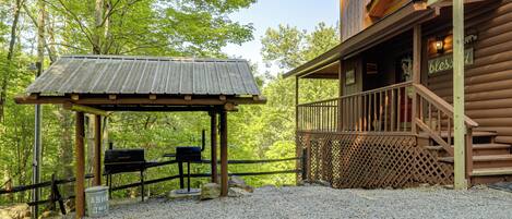 A rustic cabin with a covered outdoor seating area, a wooden deck, and a gravel ground.