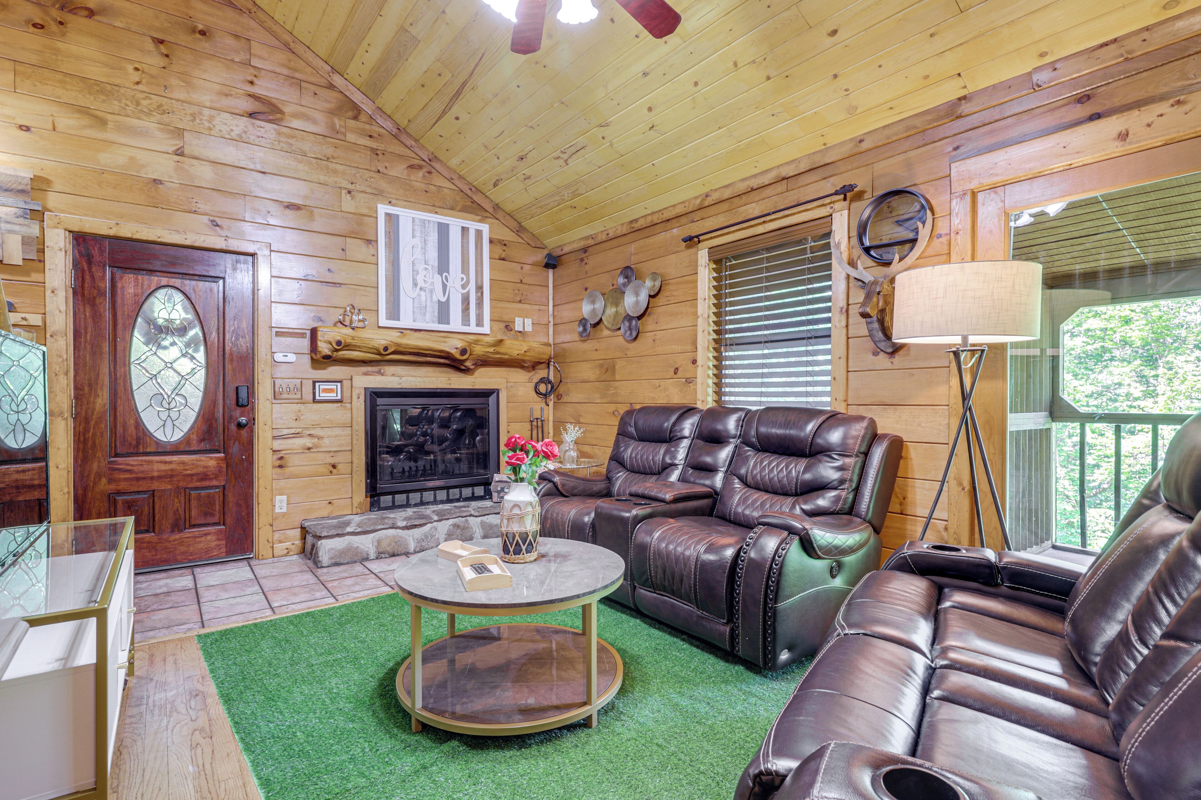 Interior de una cabaña de madera con chimenea, sofás de cuero, una mesa de centro redonda y una puerta con panel de vidrio.