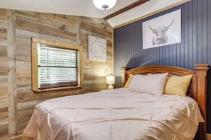 A bedroom with a wooden wall, a large bed with a headboard, a window with blinds, and a wall-mounted picture. - 4 Mi to Dollywood! Family Escape w/ Air Hockey! (Sevierville)