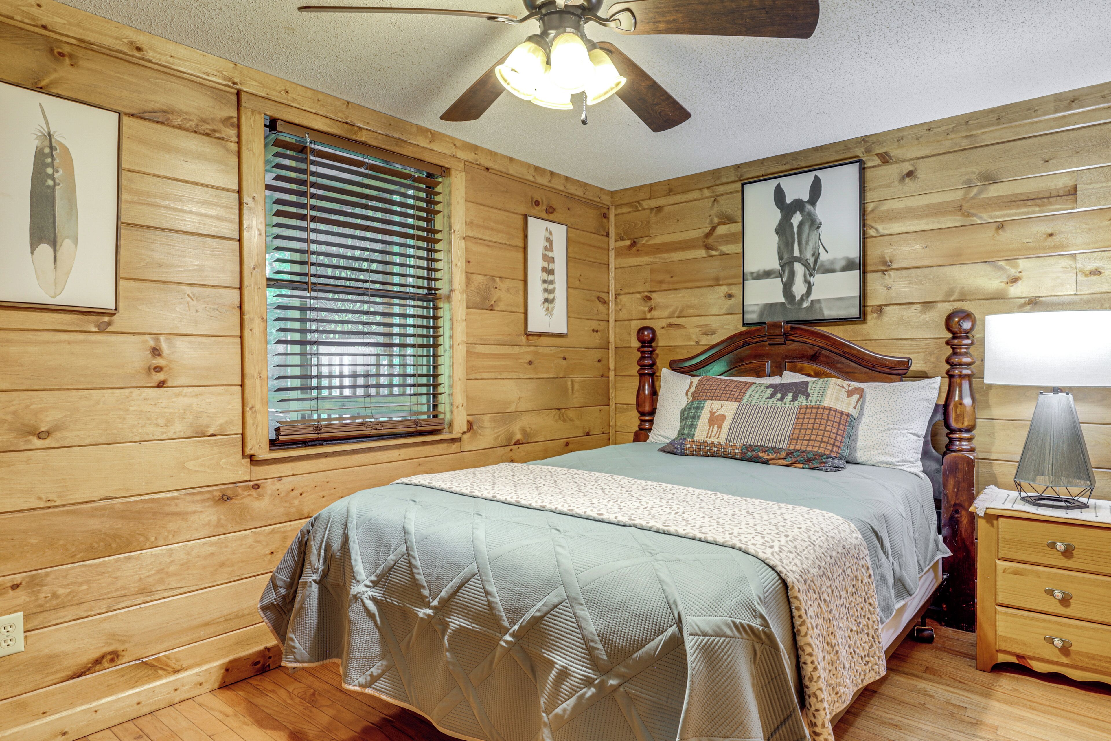 A wooden-paneled bedroom with a bed, a nightstand, a lamp, a ceiling fan, and a window with blinds.