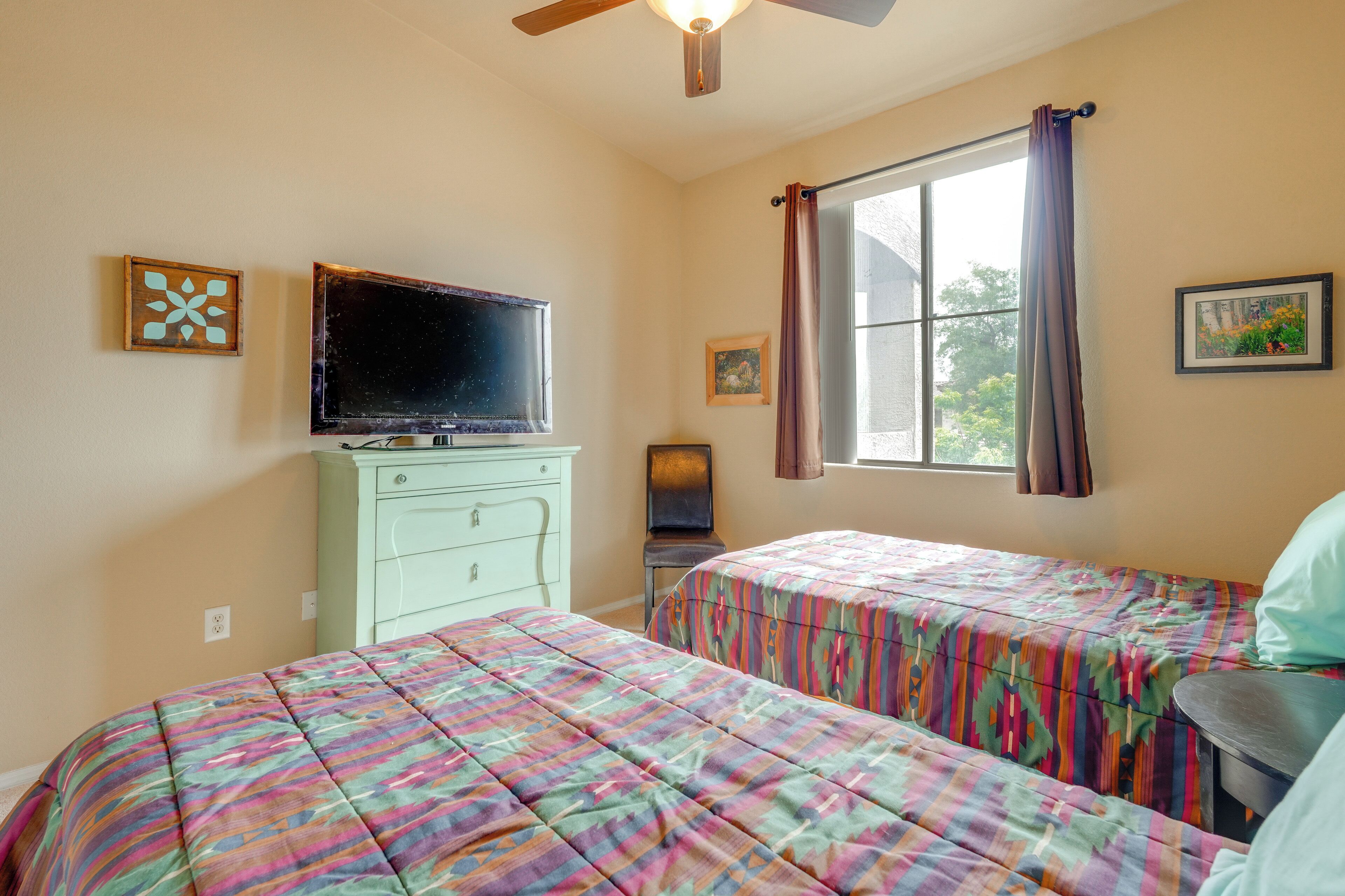 A bedroom with two beds, a dresser, a television, and a window with curtains.