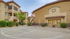 En utomhusbasketplan med en basketkorg, omgiven av bostadshus med balkonger och små träd.