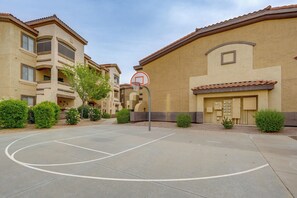 An outdoor basketball court with a hoop, surrounded by apartment buildings with balconies and small trees.