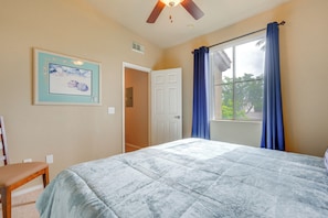 A bedroom with a bed, a chair, a ceiling fan, a window with curtains, and a door.