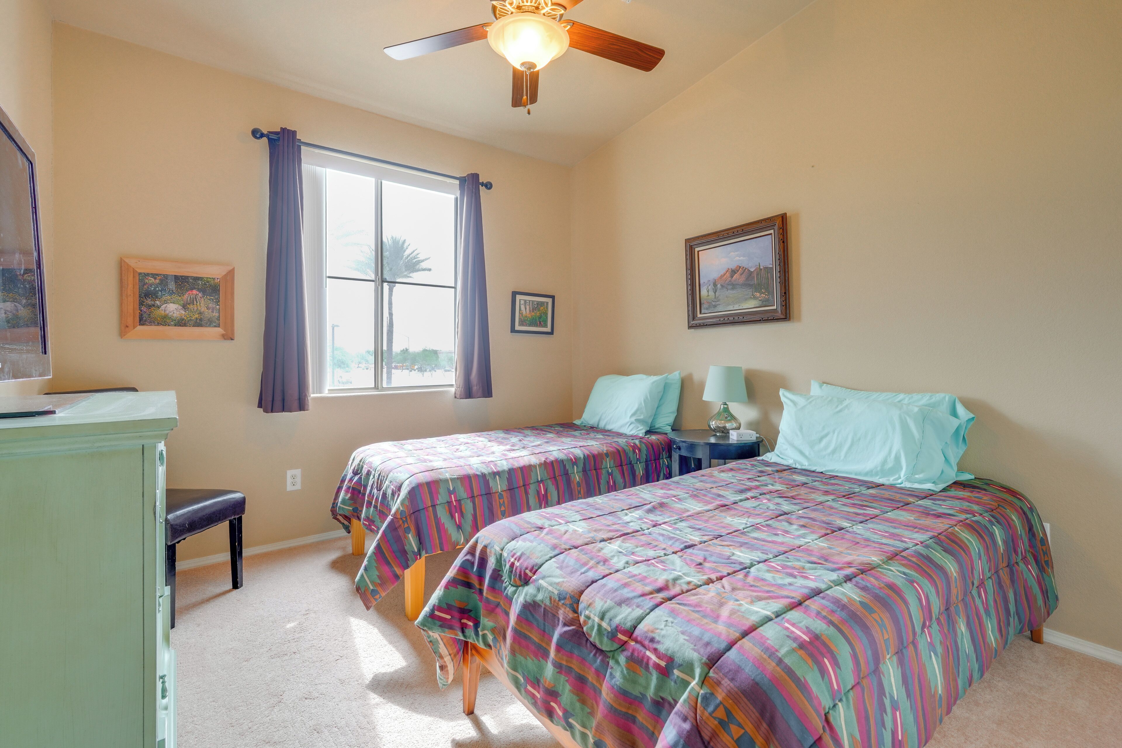 A bedroom with two beds, a ceiling fan, a window with curtains, and a desk with a chair.
