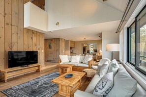 A modern living room with a flat-screen TV, wooden furniture, a sofa, and a large window. - Hike, Explore & Unwind: All-season Lincoln Retreat (Lincoln)