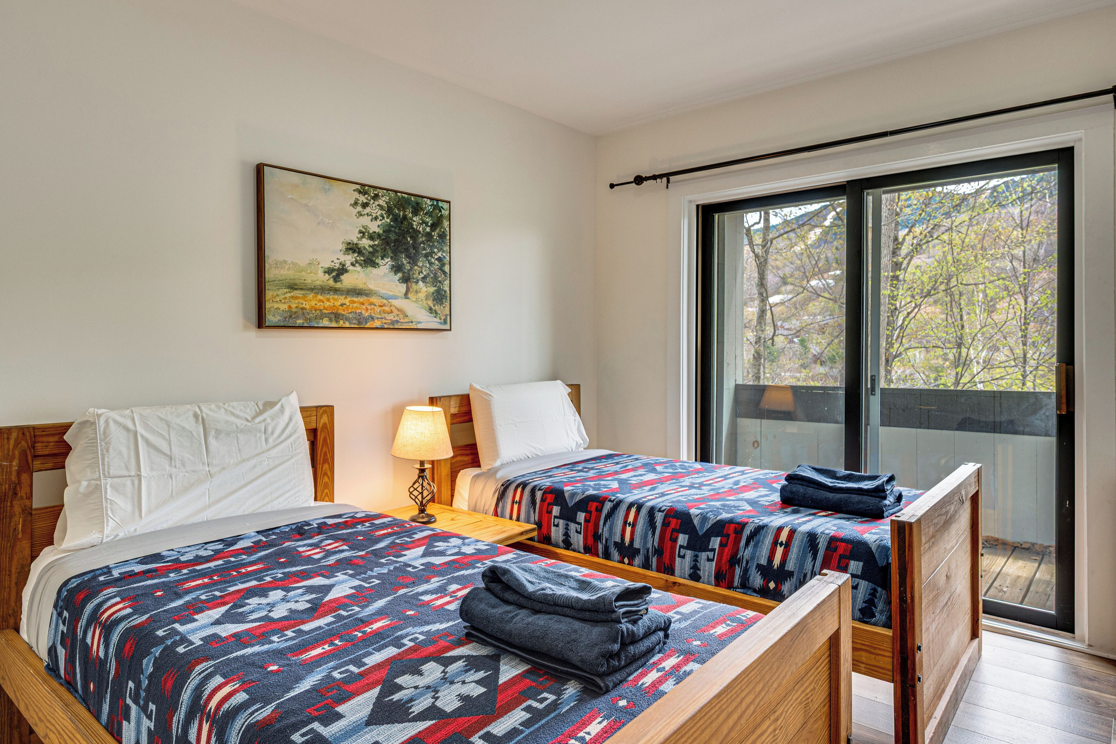 Una habitación con dos camas, un cuadro en la pared, una ventana con vistas y suelo de madera.