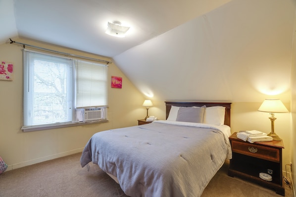 A bedroom with a bed, two bedside tables with lamps, a window with blinds, and an air conditioning unit. - Walk to Falls, Casino! Niagara Family Home w/ Yard (Niagara Falls)
