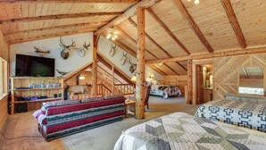 A log cabin interior with a loft bedroom, a fireplace, a television, and mounted animal heads on the wall. - Fire Pit: 20-acre Creekfront Retreat in Gunnison! (Gunnison)