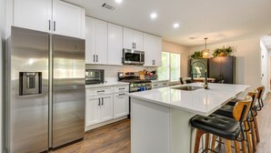 Una cocina moderna con electrodomésticos de acero inoxidable, armarios blancos, una isla grande con taburetes y un comedor con candelabro.