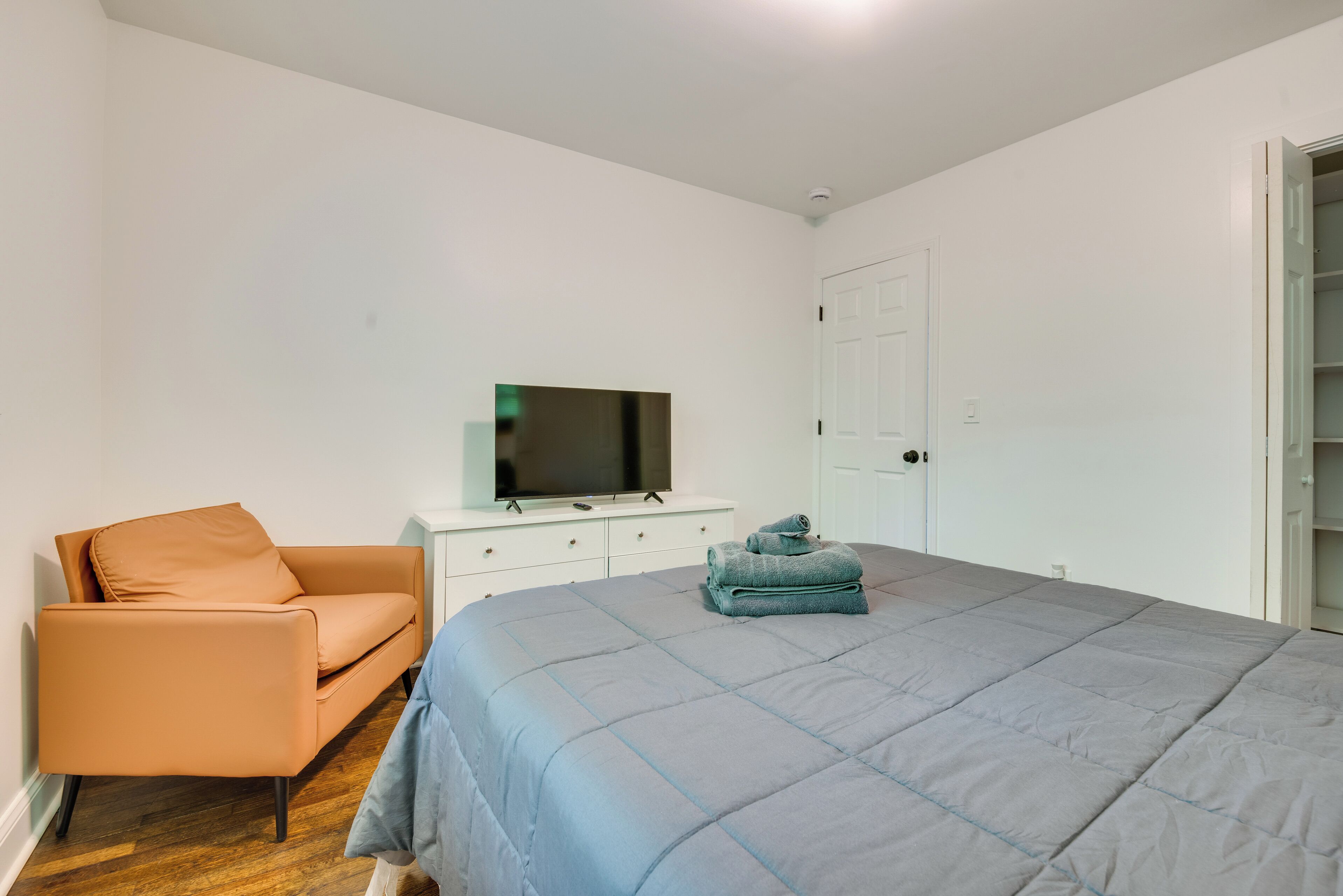 Ein Schlafzimmer mit einem Bett, einem Fernseher auf einer Kommode, einem Sessel und einer Tür.