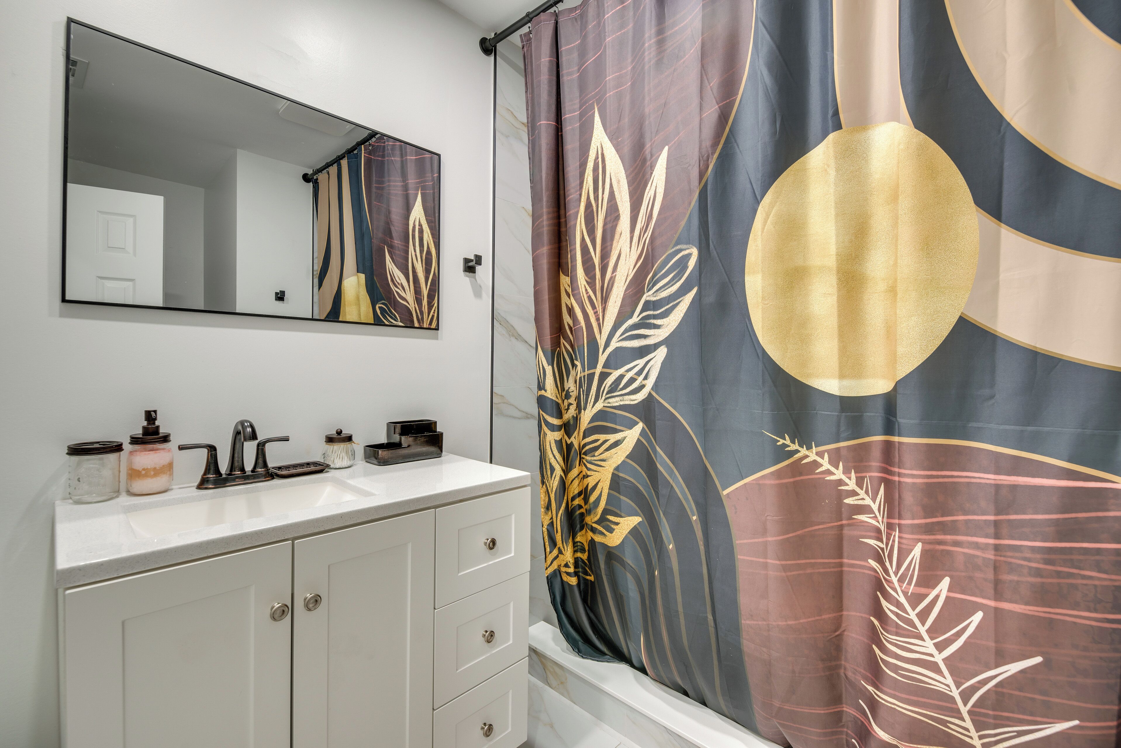 Een badkamer met een witte wastafel, een spiegel, een wastafel en een douchegordijn met een bladpatroon.