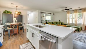 Una cocina moderna con una isla central, un comedor con sillas, un banco empotrado y un amplio ventanal con cortinas.