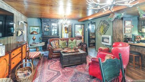 A cozy living room with a wooden ceiling, a large chandelier, a red leather sofa, a brown leather armchair, and a vintage-style coffee table.
