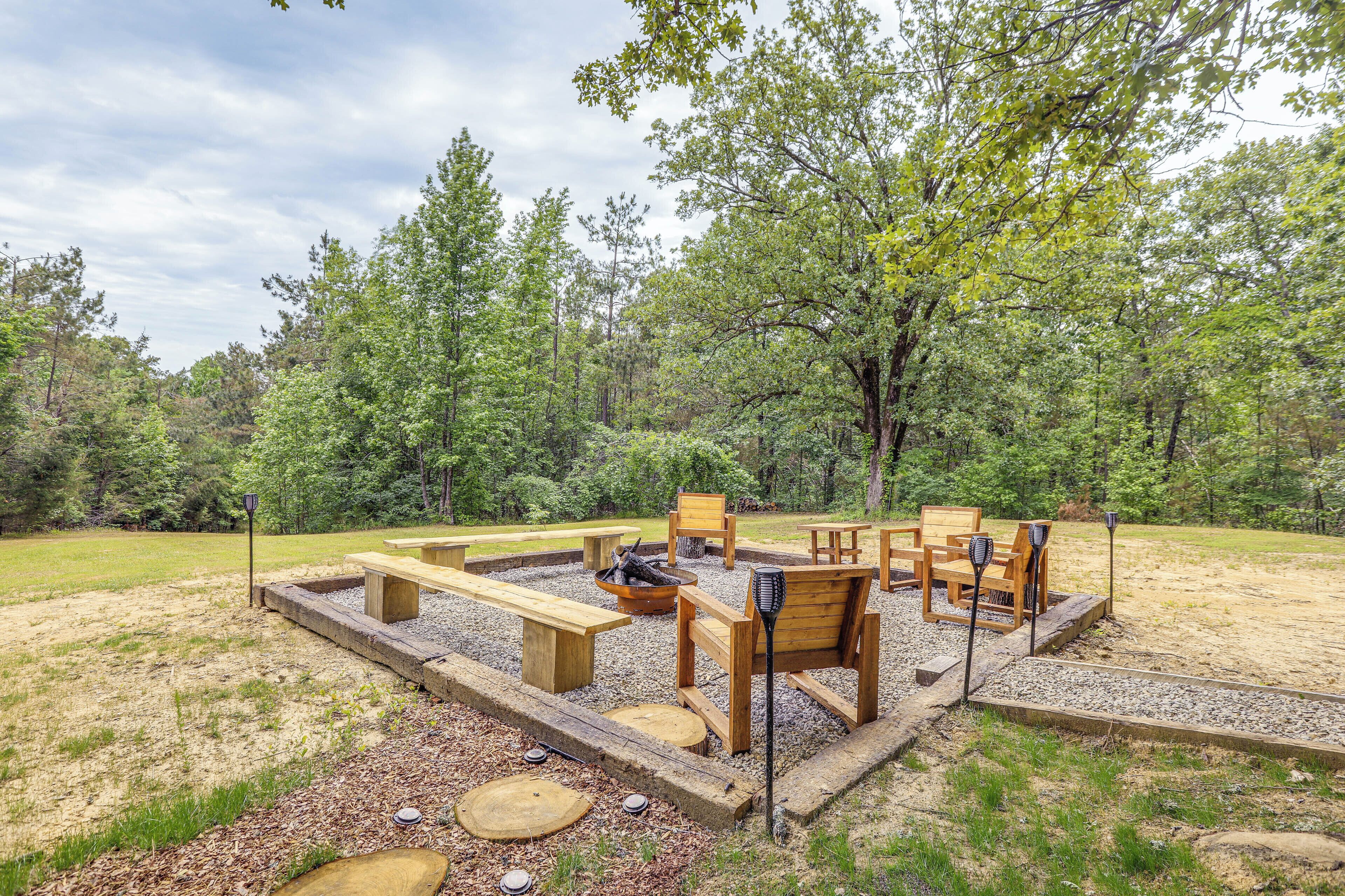 An outdoor seating area with wooden benches and tables, surrounded by trees.