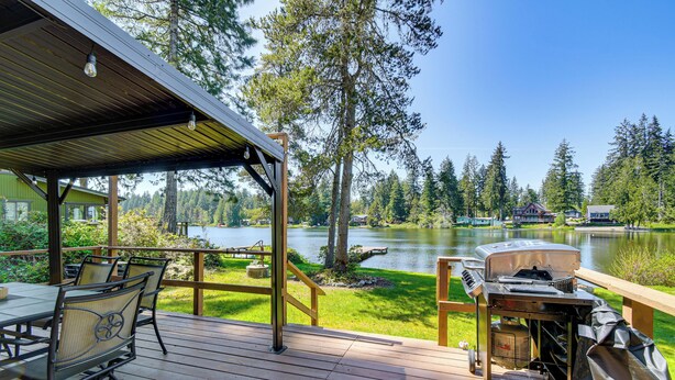 A deck with outdoor furniture, a grill, and a view of a lake surrounded by trees. - Trails End Retreat in Belfair w/ Private Dock (Belfair)