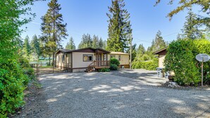 A two-story house with a gravel driveway, wooden deck, and a satellite dish. - Trails End Retreat in Belfair w/ Private Dock (Belfair)