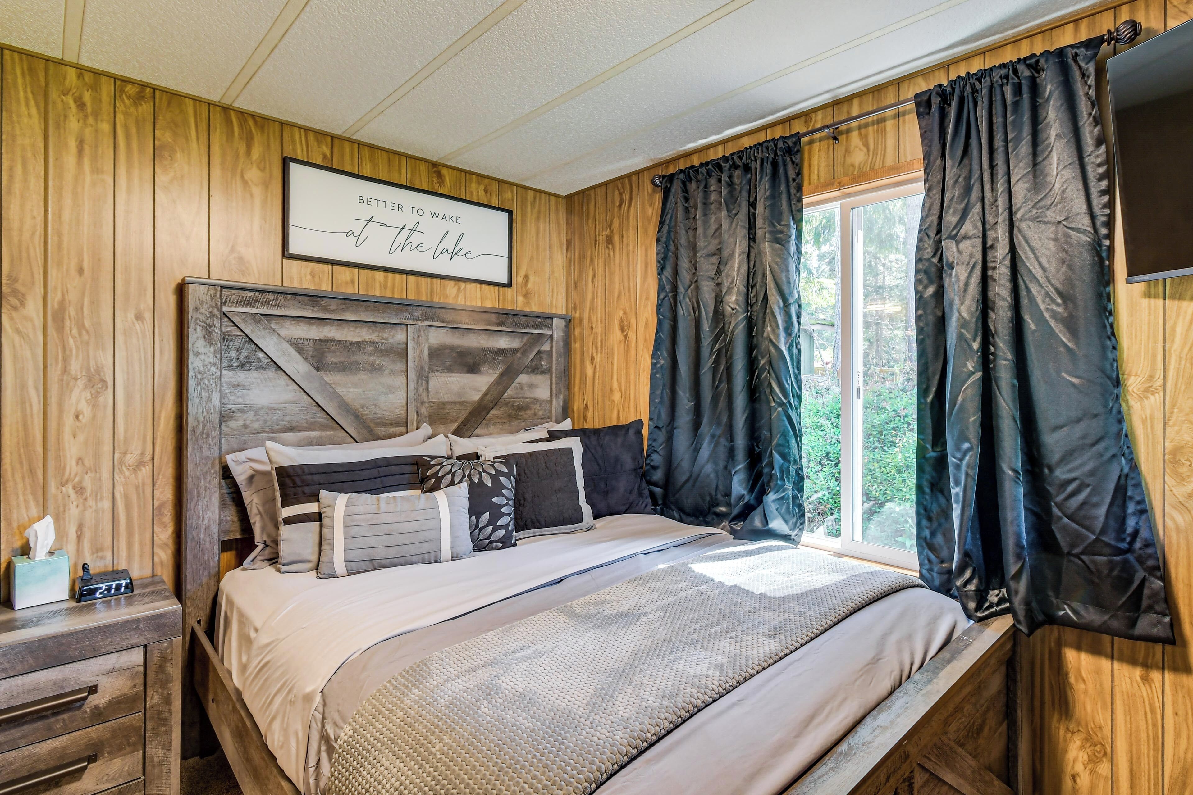 A wooden-paneled bedroom with a bed, curtains, a bedside table, and a wall-mounted sign.