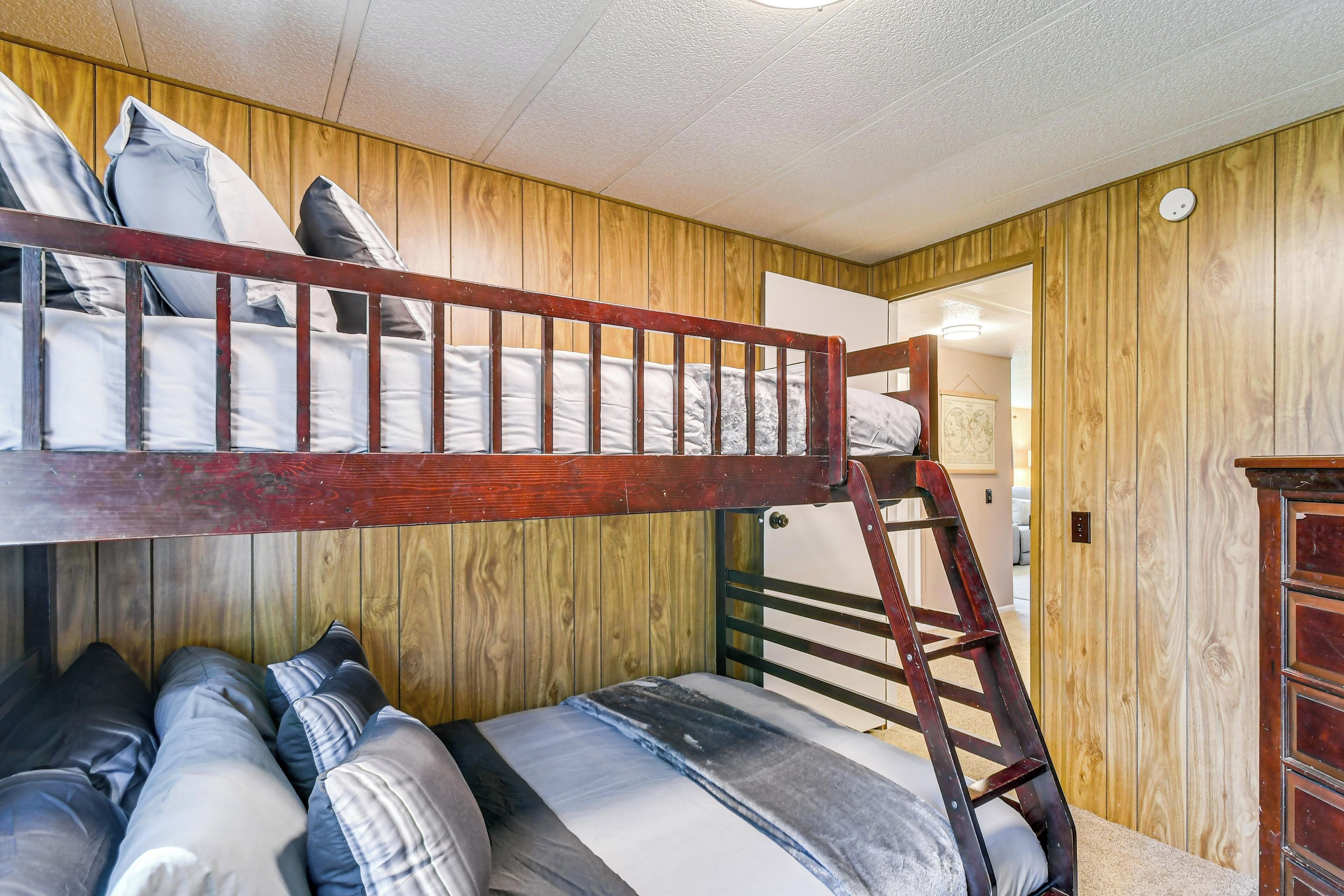 A bunk bed with a wooden ladder, a dresser, and a door leading to another room.