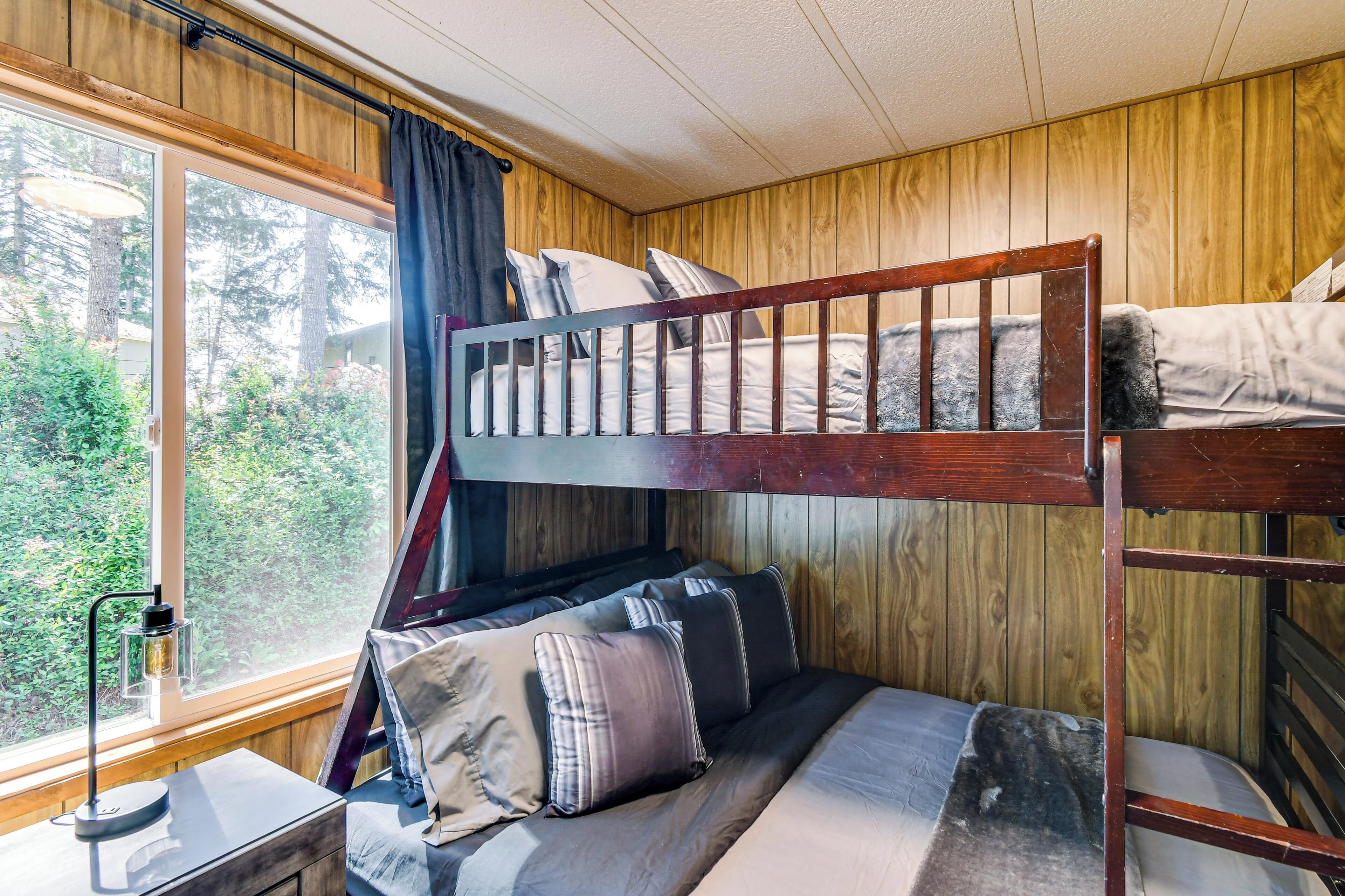 A bunk bed with a desk and chair, a window with curtains, and a view of trees.