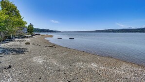 A pebbled beach with a house and trees, a calm lake, and distant mountains. - Trails End Retreat in Belfair w/ Private Dock (Belfair)