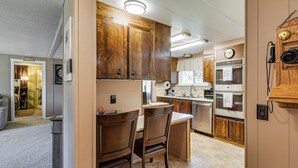 A kitchen with wooden cabinets, a dining area with two chairs, and a clock on the wall. - Trails End Retreat in Belfair w/ Private Dock (Belfair)