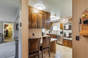 A kitchen with wooden cabinets, a dining area with two chairs, and a clock on the wall. - Private Dock & Furnished Deck! Cozy Belfair Escape (Belfair)
