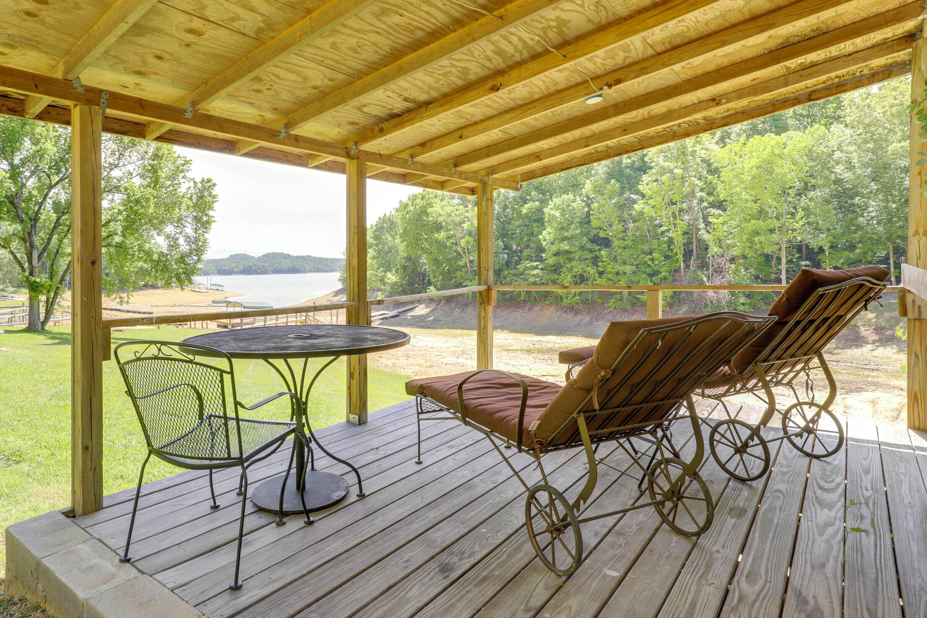 Une terrasse en bois avec une table et des chaises, offrant une vue sur une plage et une forêt.
