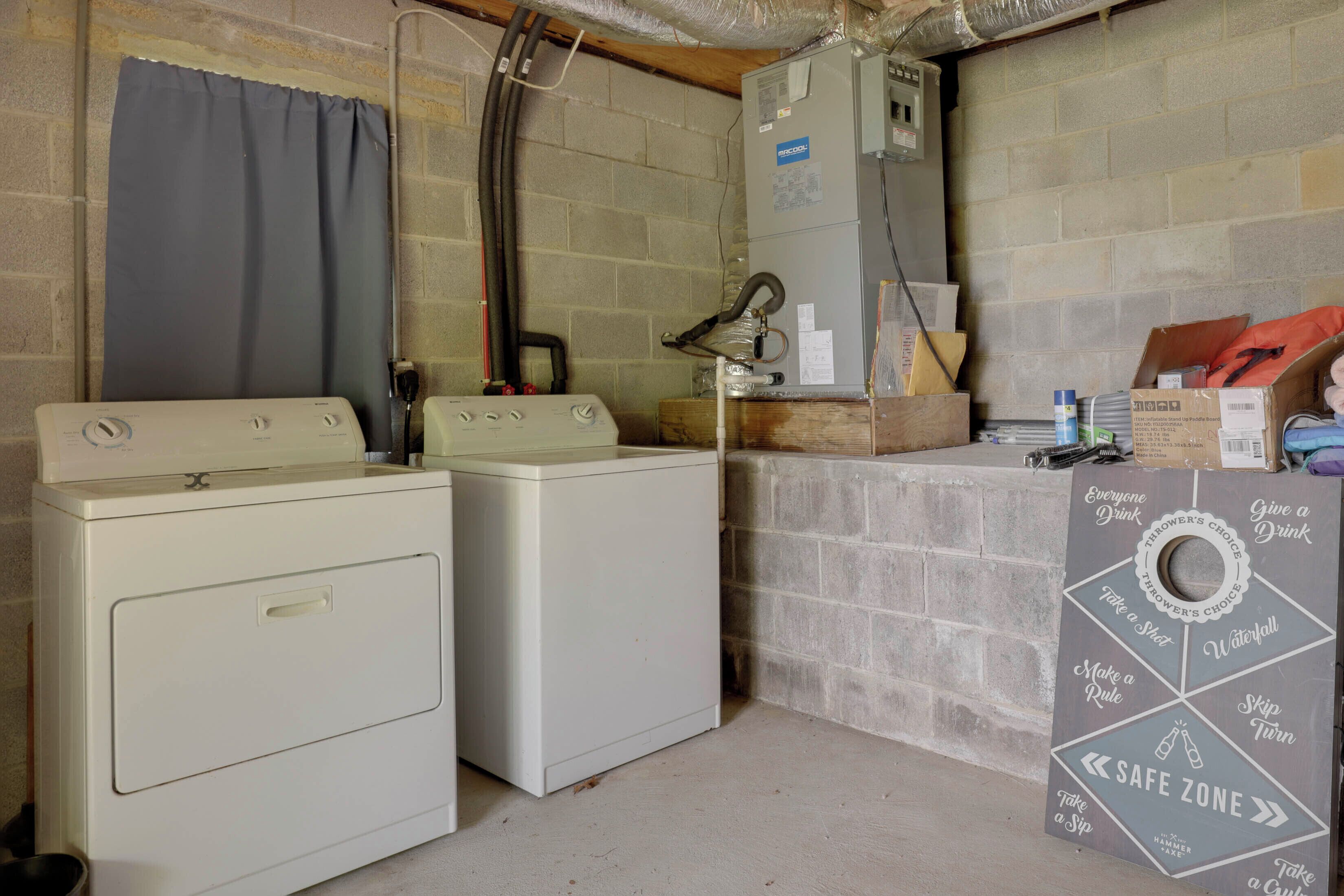 A laundry room with two washers and dryers, a water heater, and a dartboard with safety instructions.