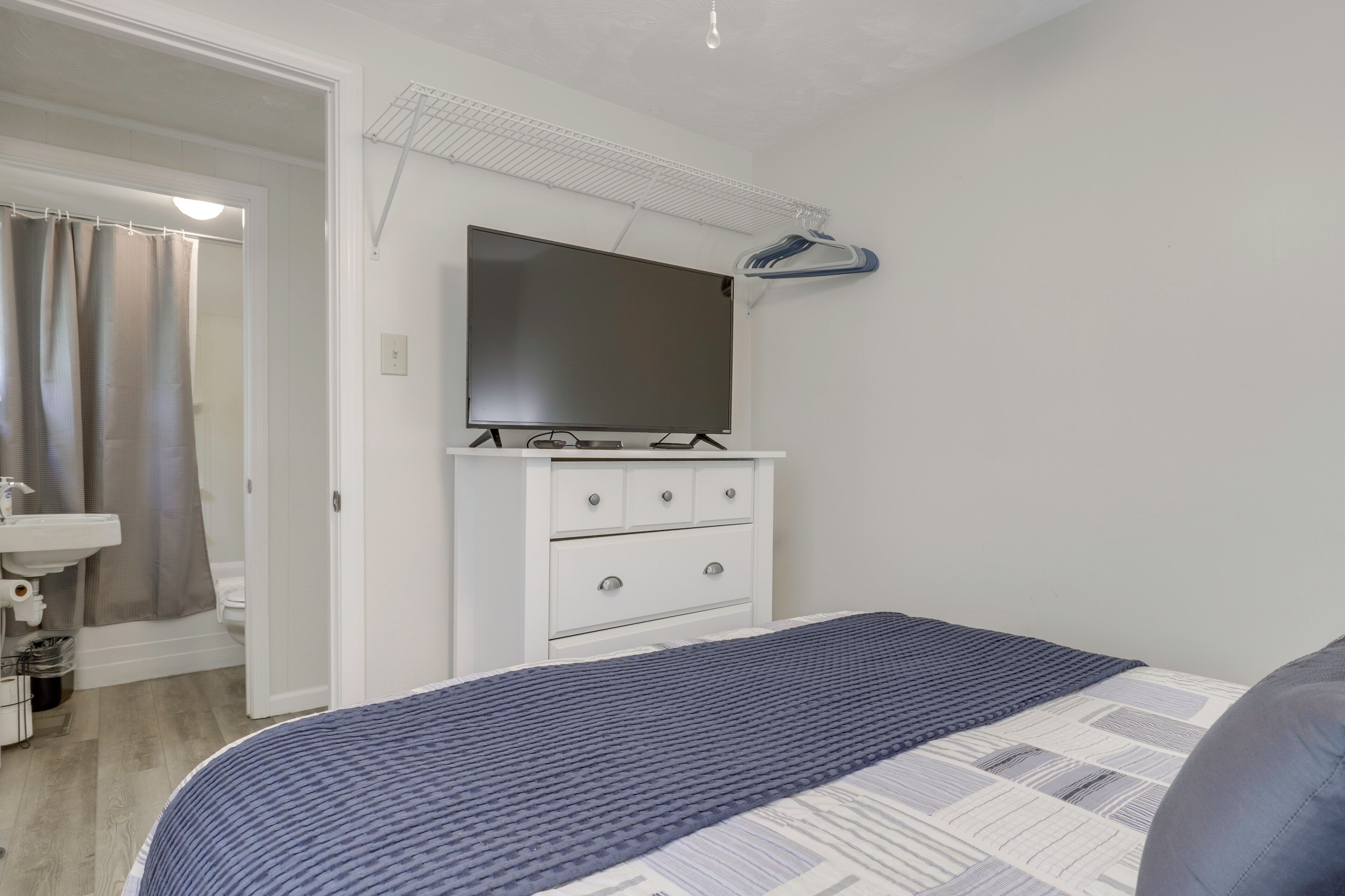 A bedroom with a bed, a dresser, a TV, and a shower area.