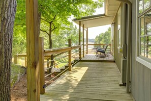 Une terrasse en bois avec une rambarde, un banc et une vue sur un lac entouré d’arbres.
