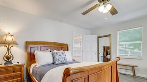 Ein Schlafzimmer mit einem hölzernen Bett, einem Nachttisch, einer Lampe, einem Deckenventilator, einem Fenster mit Jalousien und einer Tür.