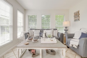 A living room with a sofa, a coffee table, and a lamp. There are windows with blinds, a wall with a sign, and a floor with tiles. - Douglas Lake Gem on Private Cove w/ Amazing Views! (Dandridge)
